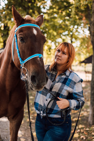 A woman stands near a horse. Farming, horseback riding. Autumn Park. High quality photo