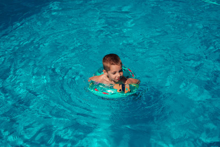A little boy with a circle bathes in clear blue water. Swimming in the pool