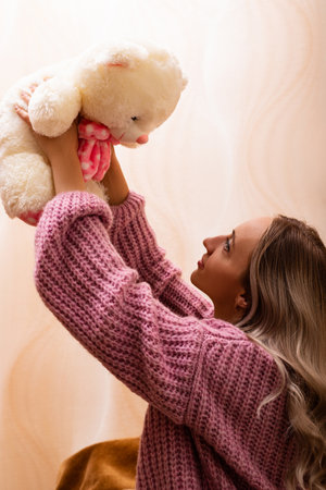 Woman sitting on sofa with teddy bear. Retro photo with plush toy. High quality photoの写真素材
