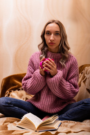 Woman with book and tea sitting on sofa. Retro style. Knowledge Day. High quality photoの写真素材