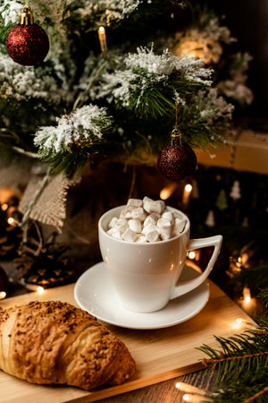 A marshmallow in a cup and a croissant stand on the table near the Christmas tree. New Year's Eve at home. High quality photoの写真素材