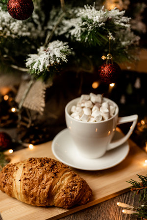 A marshmallow in a cup and a croissant stand on the table near the Christmas tree. New Year's Eve at home. High quality photoの写真素材