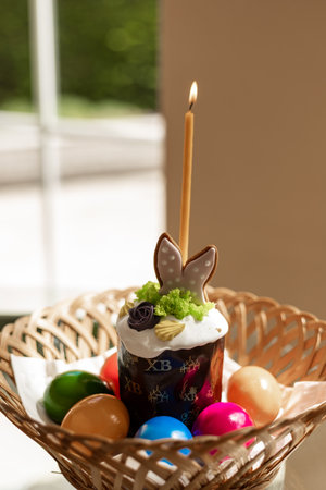 Easter cake with a lit candle. Easter colorful eggs in a basket on the table. High quality photoの写真素材