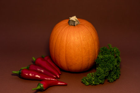 Pumpkin, chili peppers and parsley on a brown background. Composition of vegetables. Proper nutrition. High quality photoの写真素材