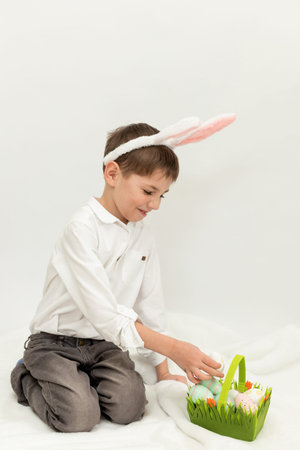 Little Boy with Easter Bunny Ears Painting Easter Eggs on White Background. High quality photo