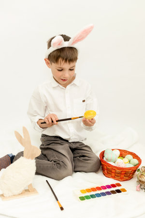 Little Boy with Easter Bunny Ears Painting Easter Eggs on White Background. High quality photoの写真素材