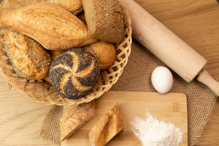 Homemade fresh pastries. Buns in a wicker basket. Flour, egg, rolling pin on the table. View from above. Homemade cakes. High quality photoの写真素材