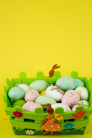 Colorful Easter eggs in a green basket on a yellow background. Easter festival. High quality photoの写真素材