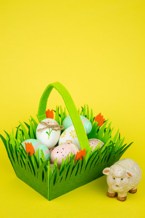 Green basket with Easter colorful eggs and sheep on a yellow background. High quality photoの写真素材