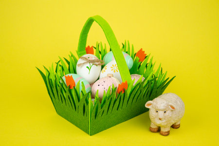 Green basket with Easter colorful eggs and sheep on a yellow background. High quality photoの写真素材