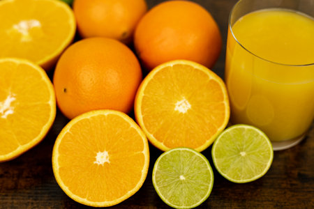 Cut oranges and limes on the table. A glass of citrus juice. Freshly squeezed orange juice. High quality photoの写真素材