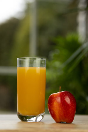 A glass of multifruit juice and an apple on the table by the window. Apple and juice.