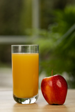 A glass of multifruit juice and an apple on the table by the window. Apple and juice. High quality photoの写真素材