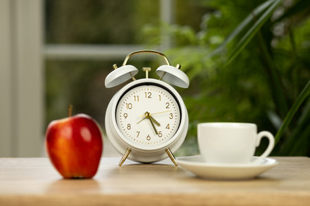 A red apple, a cup of coffee and an alarm clock on the table. Meal planning. High quality photoの写真素材