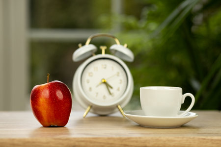 A red apple, a cup of coffee and an alarm clock on the table. High quality photoの写真素材