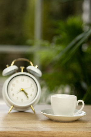 A cup of coffee, an alarm clock on the table near the window. Coffee break time. High quality photo
