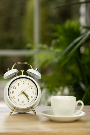 A cup of coffee, an alarm clock on the table near the window. Coffee break time. High quality photoの写真素材