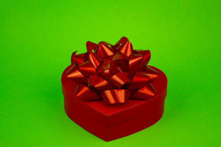 Red heart-shaped box with red bow close-up on green background. High quality photoの写真素材