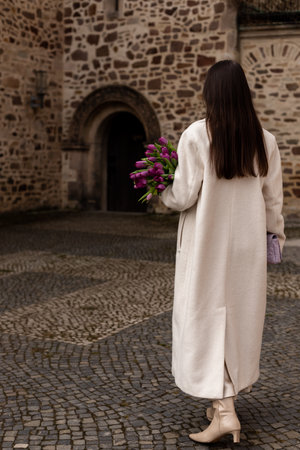 Young woman in coat with tulips. The girl stands with her back with tulips in her hands. High quality photoの写真素材