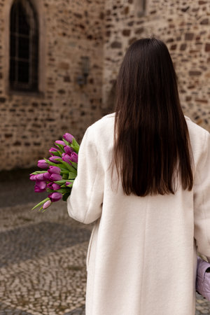 Young woman in coat with tulips. The girl stands with her back with tulips in her hands. High quality photoの写真素材