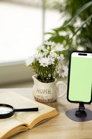A mobile phone with a green screen. Smartphone on a stand. Book with a magnifying glass. High quality photoの写真素材