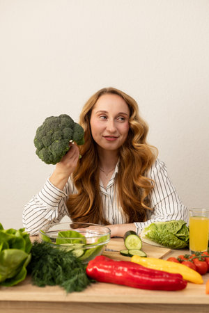 Beautiful young woman holding broccoli in her hands. Lots of fresh vegetables on the table. High quality photoの写真素材