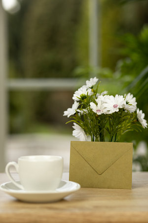 A cup of coffee, flowers and an envelope. Office desk with a cup of coffee. Desktop by the window. High quality photoの写真素材