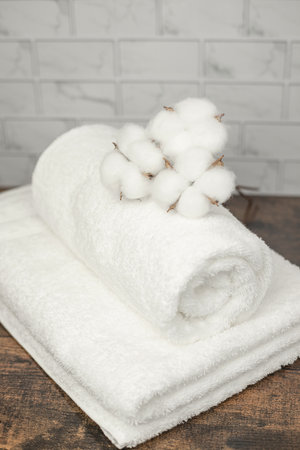 A rolled towel with a roller lies in the bathroom. Cotton flowers on white towel.の写真素材
