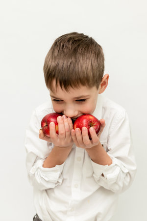 A boy bites into red apples. Boy with apples on a white background. The child eats apples. High quality photoの写真素材