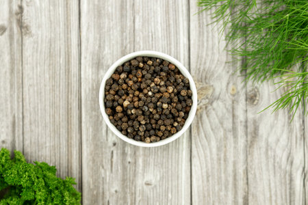 Black peppercorns in a white plate. A hot spice for cooking. Pepper, parsley, dill. Preparation for conservation. High quality photoの写真素材