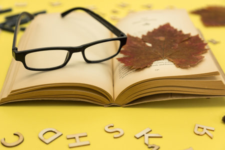 Open book with glasses on a yellow background. Autumn background associated with education.の写真素材