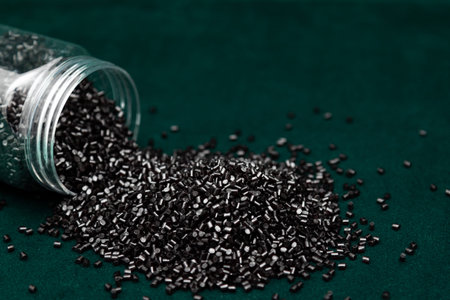 Black Plastic Granules Spilled from Jar on Green Background