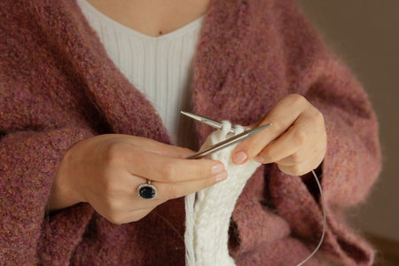 Close-up of female hands knitting with white wool yarn and metal needles, handmade craft and cozy hobby concept. High quality photoの写真素材