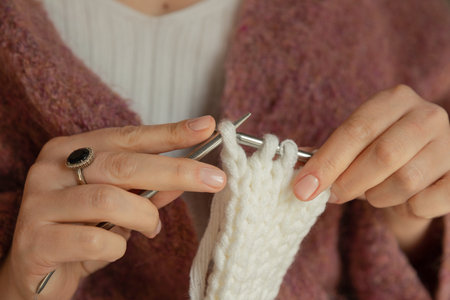 Close-up of female hands knitting with white wool yarn and metal needles, handmade craft and cozy hobby concept. High quality photoの写真素材