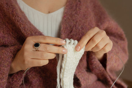 Close-up of female hands knitting with white wool yarn and metal needles, handmade craft and cozy hobby concept. High quality photoの写真素材