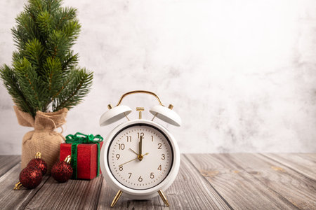 Christmas composition with a white alarm clock, red gift box with green ribbon, and small fir tree...