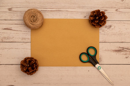 Creative flat lay composition with blank golden paper, scissors, pine cones, and jute rope on a wooden background. Ideal for craft blogs, DIY projects, or handmade Christmas designs.の写真素材