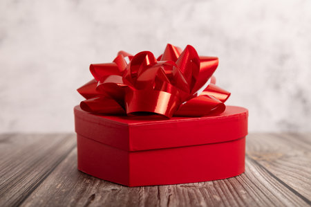 Elegant red heart shaped gift box with glossy ribbon bow on rustic wooden background. Perfect for Valentine's Day, Christmas, anniversaries, and romantic celebrations.の写真素材