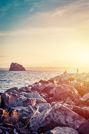 Silhouettes of men fishing from a breaker in the dusk.の写真素材