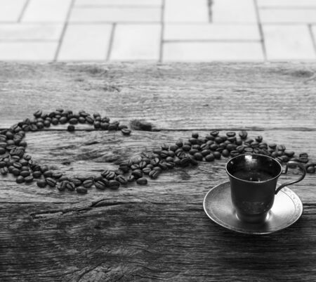 Black and white photo of a silver espresso cup and coffee beans on wooden table. Toned imageの写真素材