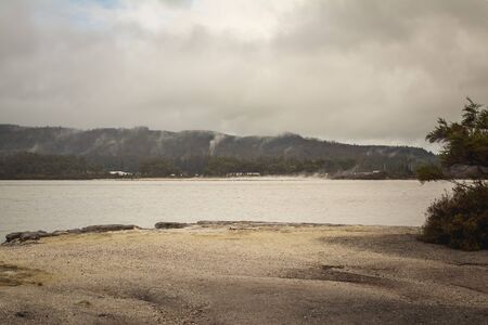 Rainy day at lake Rotorua. Sandy beach leading to grey water and steam coming up from hot pools at the distance. Rotorua, New Zealandの写真素材