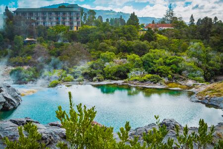 Small geothermal lake surroubded by low trees and shrubbery. Abandoned hotel building at the distance. North Island, New Zealandの写真素材