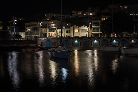Quiet night over city marina. Small sailing boat moored in front of row of colourful barns. Wellington, New Zealandの写真素材