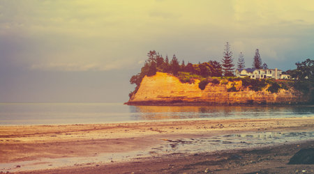 Vintage photo of iconic New Zealand landscape -a house on the green cliff over blue sea. Toned image