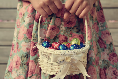 Retro style photo of girls hands holding a a small basket full of colourful Easter eggs