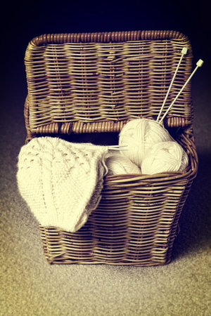 Vintage image of wicker basket with an open lid, filled with yarn rolls, knitting needles and...