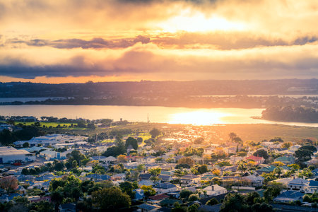 Golden sunset in a cloudy sky reflected in the clam waters of Auckland Harbour near historical...