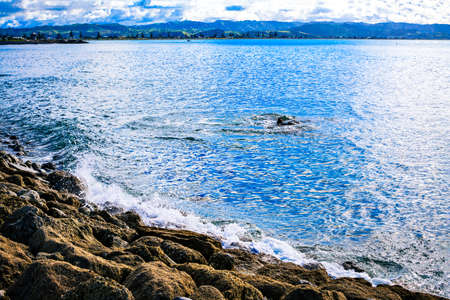 Waves crashing on stony beach. Mountain coastline in the background. Hawkes Bay, New Zealand.の写真素材