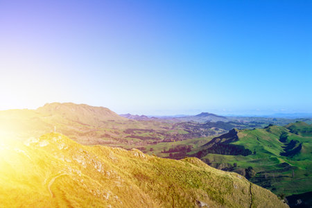A tourist on a mountain peak looking over vast green valley and enjoying beautiful summer mountain landscape. A panoramic view of Te Mata Hills iin Hawke's Bay, New Zealand.の写真素材