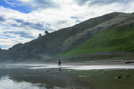 A pair of surfers walking over wet sand at Makorori Beach, mist rising over water obscuring distant mountains. Gisborne, New Zealandの写真素材